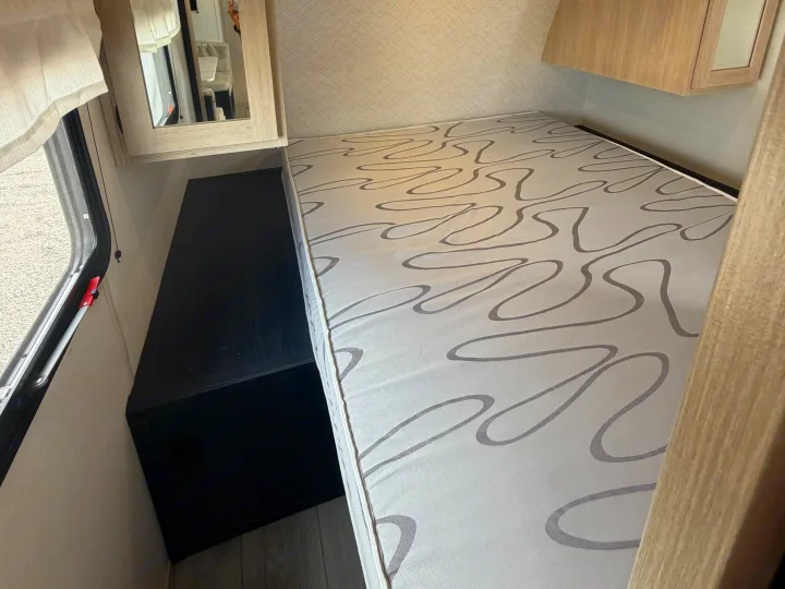 Cozy RV rental interior: bed with patterned mattress, dark storage unit, mirrored cabinet, and window with a curtain.. Avenger Avenger Trailer 2026