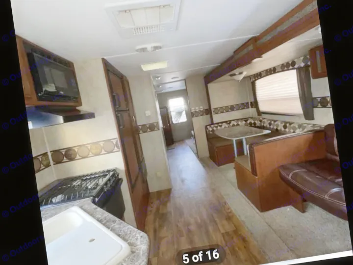 RV rental interior showing kitchen with stove/sink, dining booth, & living area with couch. Wood flooring throughout.. Keystone RV Passport Ultra Lite 2015