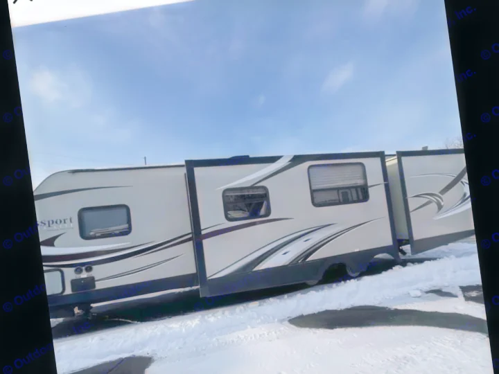 Spacious RV rental, a light-colored travel trailer with extended slide-outs, parked in snow under a blue sky.. Keystone RV Passport Ultra Lite 2015