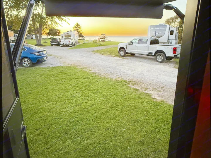 RV park sunset view from an RV: white truck, Reflection RV, blue car, and lakeside playground. Ideal for your RV rental.. Keystone Coleman 13b 2027