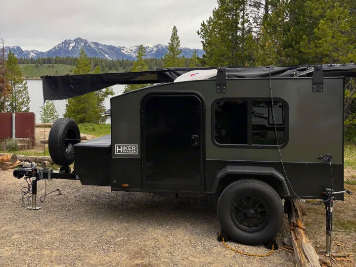 Hiker Trailer teardrop RV rental at a scenic mountain-lake campsite, ready for adventure under an overcast sky.. Hiker 5x8 Highway Deluxe 2025