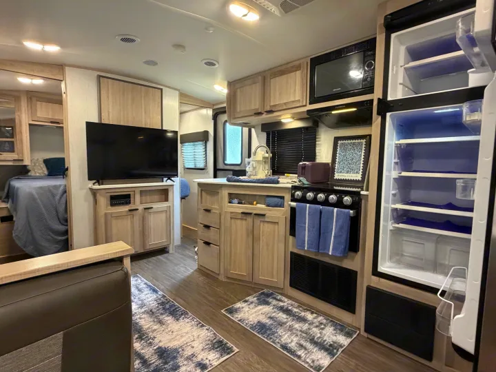 Modern rv rental interior with kitchen, living space, and bed. Open fridge, oven, TV, and light wood cabinets.. Cruiser RV Shadow Cruiser 2022