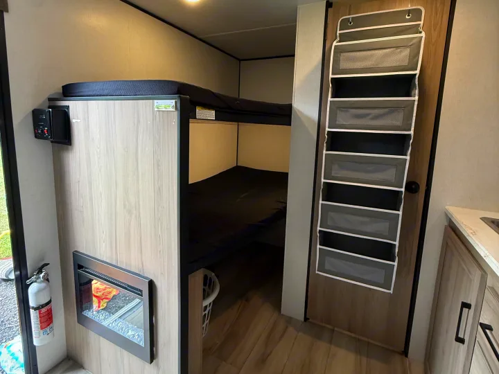 This RV rental interior showcases bunk beds, a cozy fireplace, and a hanging organizer maximizing compact living space.. Keystone Coleman 13b 2027