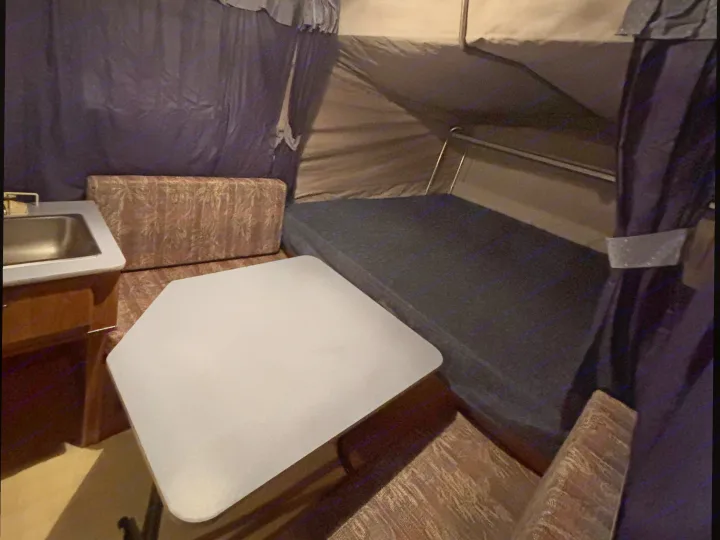 This RV rental interior features a compact sink, a hexagonal dining table, and a sleeping area with a dark mattress and canvas walls.. Starcraft Travel Trailer 1994