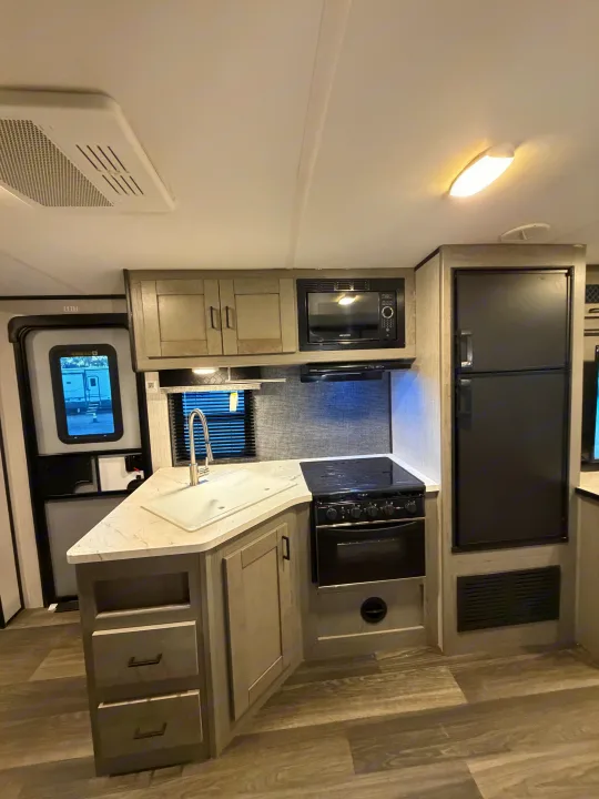 Modern RV rental kitchen with sink, stove, microwave, and fridge. Perfect for road trips and camping.. Heartland RVs Mallard 2021