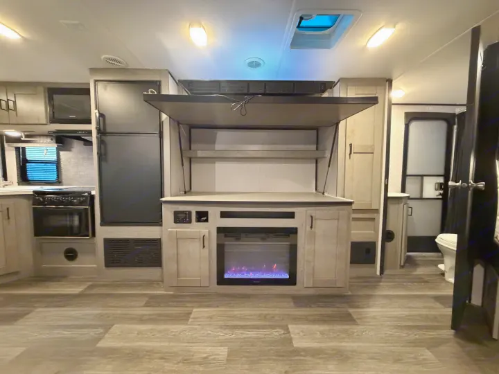 RV rental interior: kitchen with fridge, fireplace entertainment unit with lifted bed/storage, and bathroom door.. Heartland RVs Mallard 2021