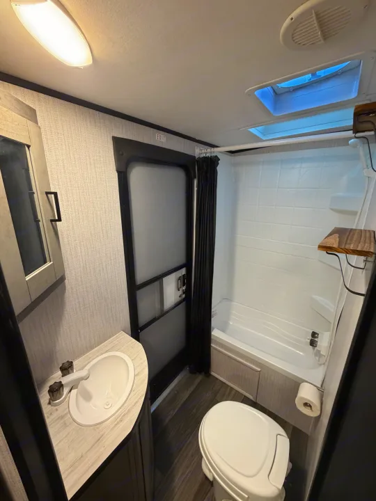 This RV rental's compact bathroom includes a sink, toilet, and shower/tub unit with wood-look shelves.. Heartland RVs Mallard 2021