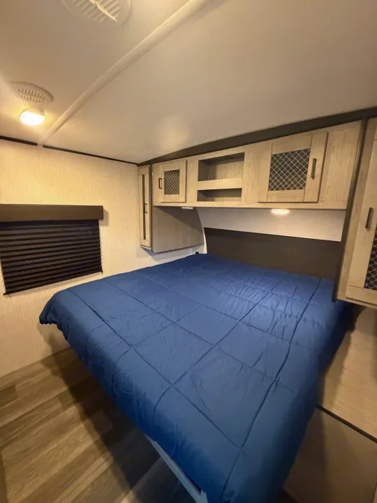 Cozy RV rental bedroom with blue comforter, overhead storage, and window blind for comfortable travel.. Heartland RVs Mallard 2021