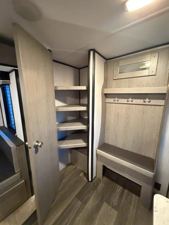 This RV rental interior features a modern bench with coat hooks and mirror, plus a corner pantry with shelves for storage.. Heartland RVs Mallard 2021