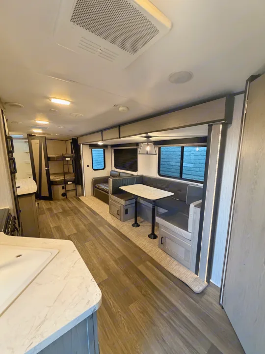 Explore this modern RV rental interior featuring a kitchen counter, dining booth, comfortable sofa, and rear bunk beds.. Heartland RVs Mallard 2021