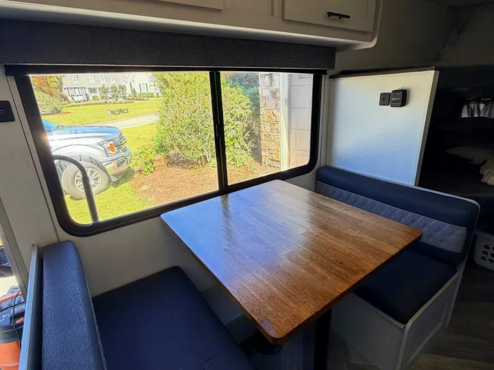 RV rental dinette features a wooden table and blue bench seats, offering a view of a residential street outside.. Forest River Salem FSX PLATINUM 2021