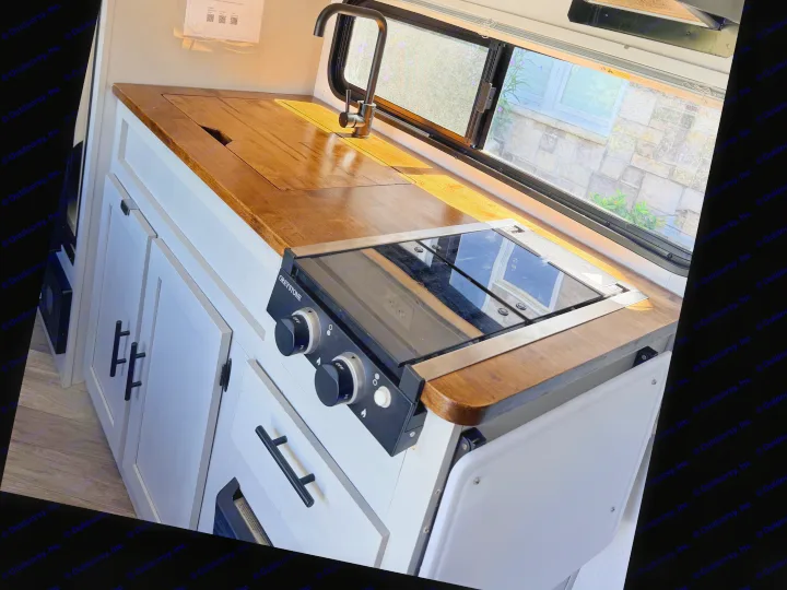 Functional rv rental kitchen with a sleek wooden countertop, black faucet, and GREYSTONE stove. White cabinets below.. Forest River Salem FSX PLATINUM 2021