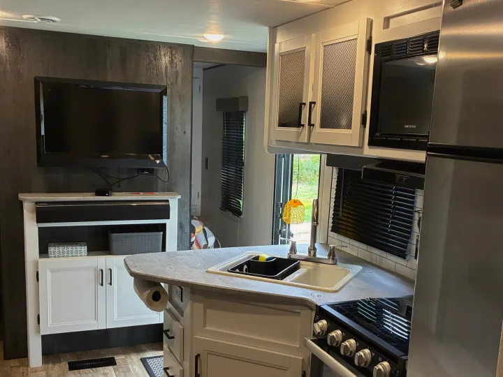 Modern RV rental interior showing a full kitchen with an island sink, microwave, stove, and a living area with a TV.. Keystone RV Hideout 2022