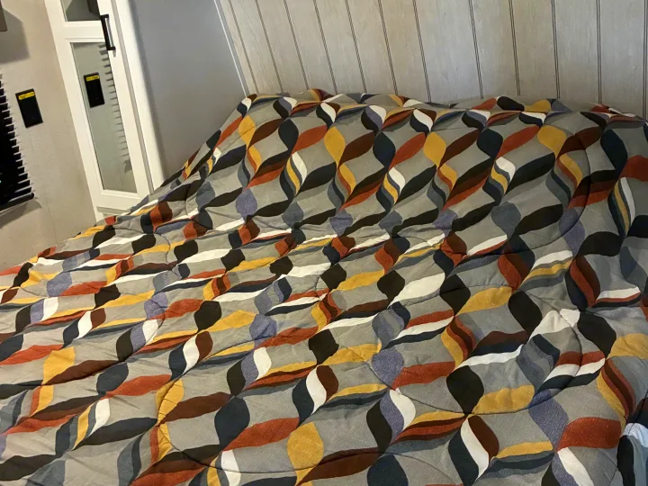 RV rental cozy bedroom with a striking abstract patterned comforter in grey, yellow, brown, and blue tones.. Keystone RV Hideout 2022