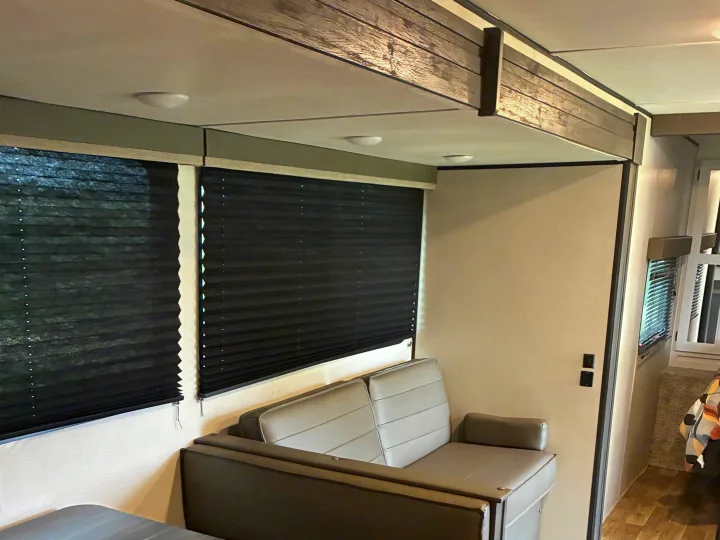 Cozy RV rental interior featuring a comfy light-colored couch, dark pleated window blinds, and overhead lighting. Enjoy this cozy space!. Keystone RV Hideout 2022