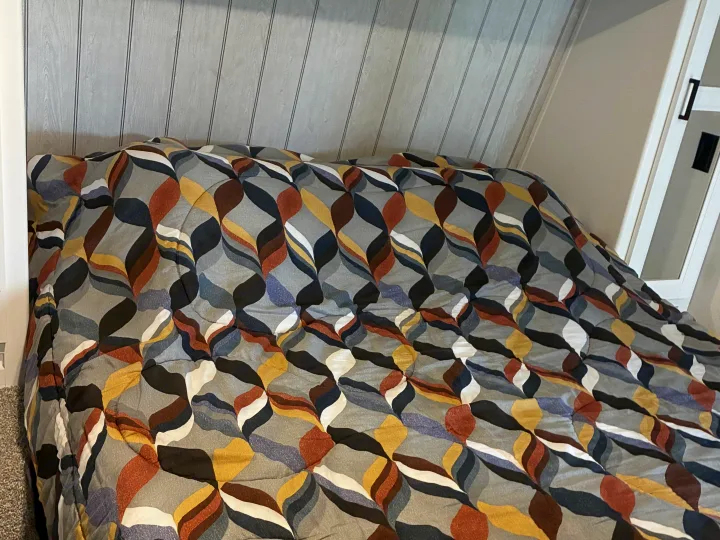 Cozy RV rental bed featuring a colorful, patterned comforter and light wood-paneled wall, perfect for a comfortable stay.. Keystone RV Hideout 2022