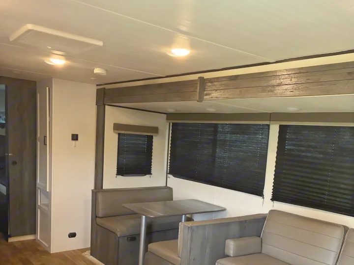 RV rental interior: modern dining area with a U-shaped dinette, table, and dark pleated window blinds under bright ceiling lights.. Keystone RV Hideout 2022