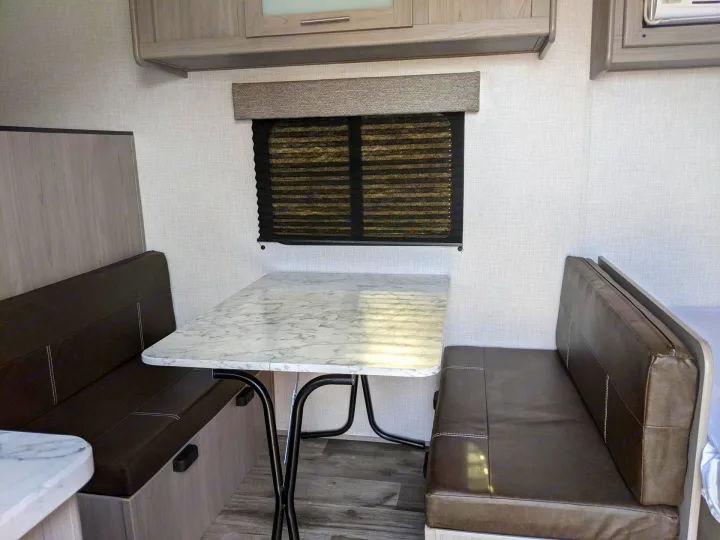 RV rental interior: A cozy dinette features dark brown benches, a light marble-patterned table, and window blinds.. Coleman Lantern 17b 2023