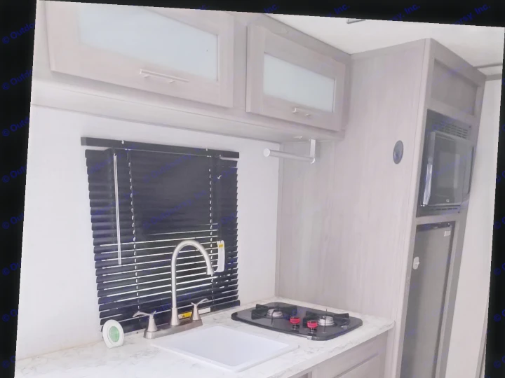 Modern RV rental kitchen: light wood cabinets, sink, two-burner stove, microwave, and mini-fridge for comfortable travels.. Dutchmen Coleman Lantern 2022