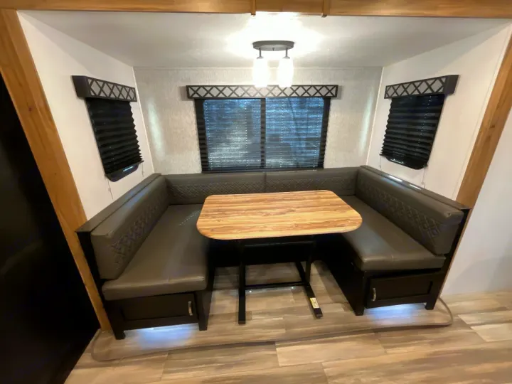 This RV rental features a cozy dinette with dark gray U-shaped booth seating, a wooden table, and three windows.. Coachmen Freedom Express 2022