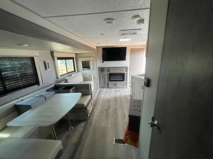 View inside a modern RV rental, showing a comfortable dining booth, entertainment center with TV/fireplace, and light flooring.. Coachmen Catalina Legacy Edition 2024