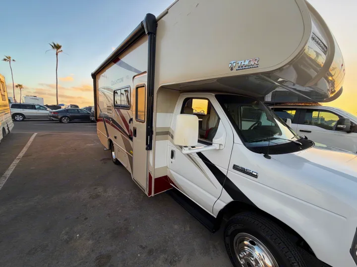 A beige and white Thor Quantum RV rental (Class C) parked at sunset with palm trees, ready for camping adventures.. Thor Quantum 2018