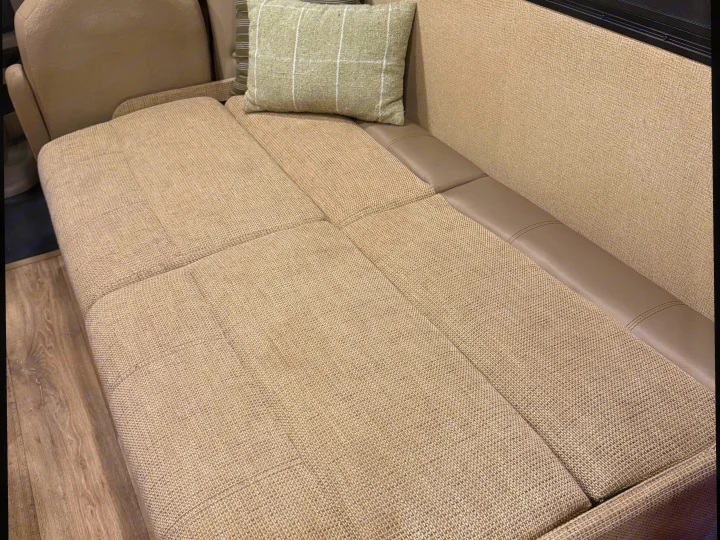 RV rental interior showing comfortable beige fabric dinette seating, likely convertible to a bed, with a green plaid pillow.. Thor Freedom Elite 2017