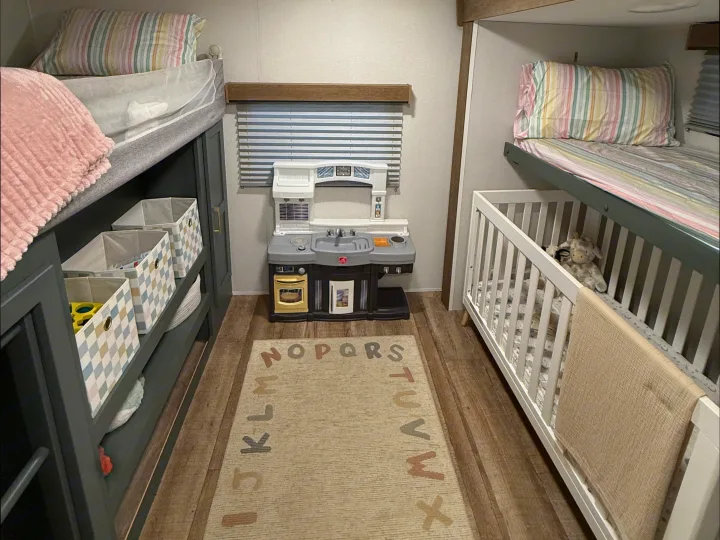Cozy RV rental interior with bunk beds, a crib, toy kitchen, and an alphabet rug, perfect for family adventures.. Heartland RVs Eddie Bauer 2026