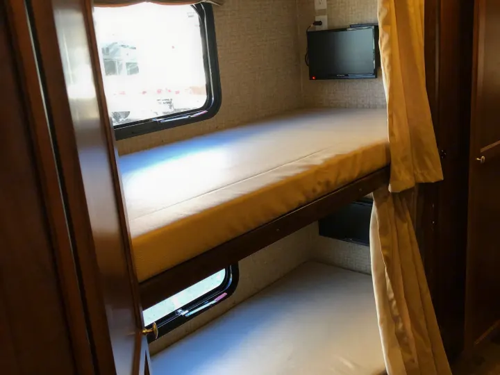 Inside this RV rental are cozy bunk beds, complete with a window and a wall-mounted TV, offering comfortable sleeping arrangements.. Coachmen Mirada 340BHS 2016