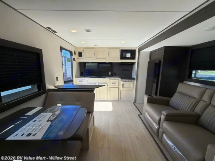 Modern RV rental interior showcasing a kitchen, dining booth, and reclining living area with dark blinds and wood-look flooring.. Coachmen Shasta 2027