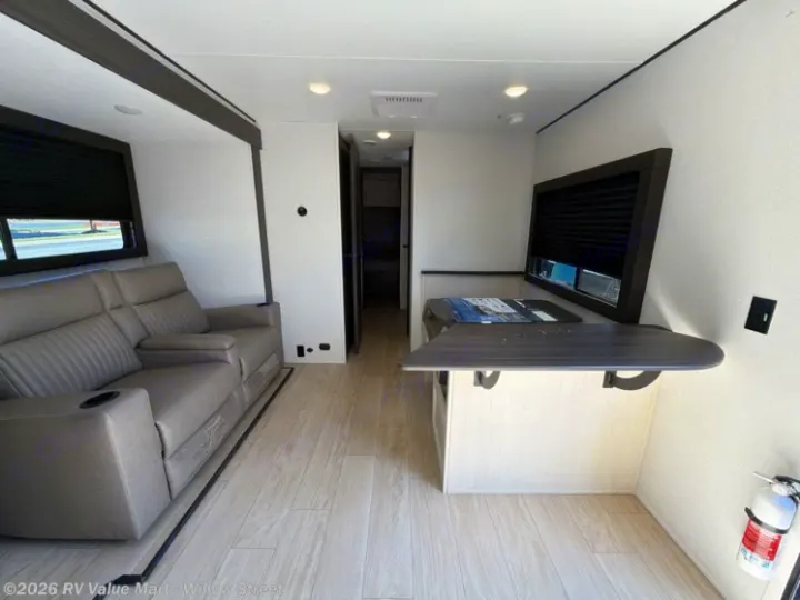 Explore this bright RV rental interior featuring a gray reclining sofa, a window-side dining table, and light wood floors.. Coachmen Shasta 2027