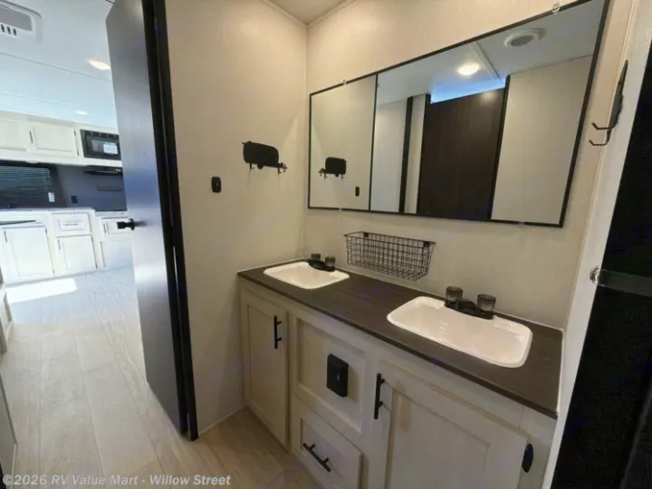 Step inside this rv rental's modern bathroom, featuring a dual-sink vanity, large mirror, and light cabinetry, with the kitchen in view.. Coachmen Shasta 2027