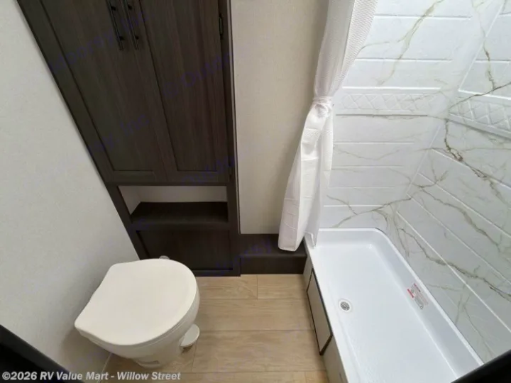 RV rental bathroom with a white toilet, dark wood cabinet storage, and a stylish shower stall with a marble-look wall.. Coachmen Shasta 2027