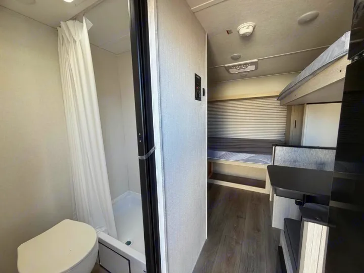 This RV rental interior features a compact bathroom with a toilet and shower, and a living area with bunk beds and a bed/dinette.. Coachmen Shasta 2027