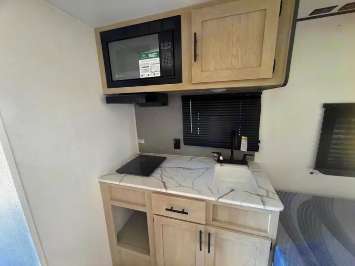 RV rental: A modern compact kitchen with microwave, sink, induction cooktop, and light wood cabinets, ready for use.. Coachmen Shasta 2027