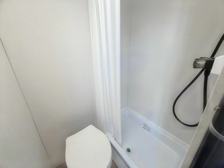 Compact RV rental bathroom features a white toilet, shower with curtain, and light gray textured walls.. Coachmen Shasta 2027