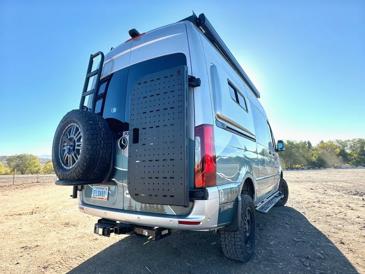 An off-road Mercedes Sprinter rv rental, customized with a ladder, spare tire, and custom graphics, parked outdoors on a sunny day.. Mercedes-Benz Sprinter 2023