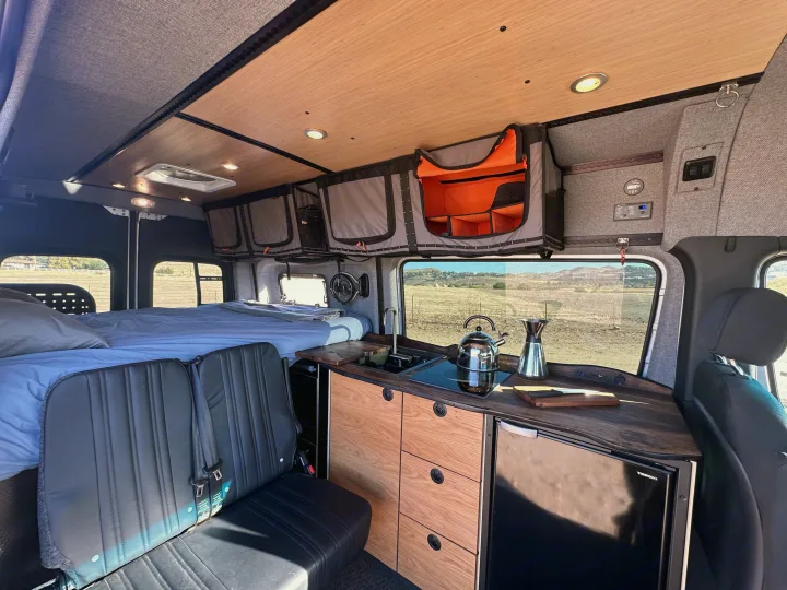 rv rental: well-appointed camper van interior with cozy bed, full kitchen, and smart overhead storage for your adventure.. Mercedes-Benz Sprinter 2023