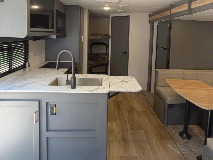 RV rental interior: well-equipped kitchen with marble-look counters, dinette, fridge, and bunk bed area.. Keystone RV Bullet Crossfire 2024