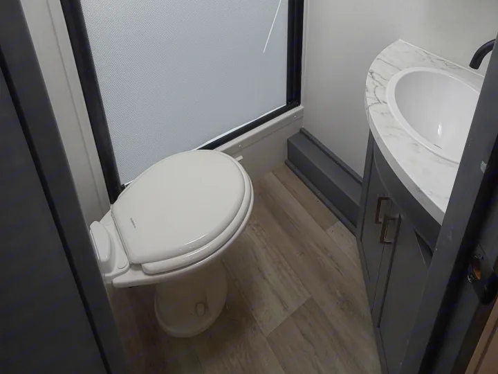 Compact rv rental bathroom with white toilet, marble vanity, and sink, showcasing the functional interior design.. Keystone RV Bullet Crossfire 2024