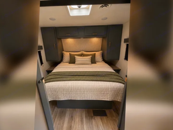 This cozy RV rental bedroom features a bed with olive throw, dark grey cabinets, and a stylish patterned headboard.. Keystone RV Bullet Crossfire 2024
