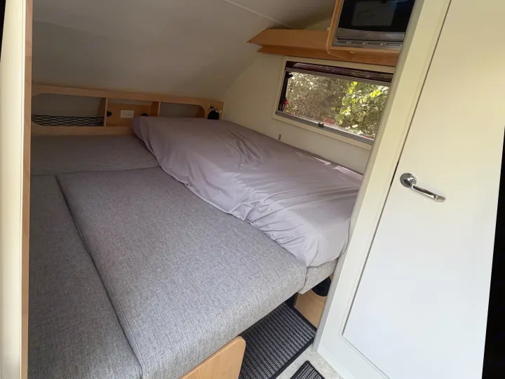 The compact interior of an rv rental features a bed, a window with foliage view, microwave, and storage cubbies.. nuCamp T@B 2026