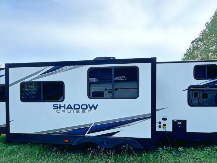 This Shadow Cruiser RV rental, a travel trailer with an extended slide-out and bold graphics, is parked on grass under a blue sky.. Cruiser RV Shadow Cruiser 2022