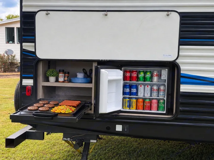 RV rental outdoor kitchen setup: grill cooking burgers/dogs, mini-fridge stocked with drinks. Ideal for camping & travel.. Heartland RVs Prowler 2022