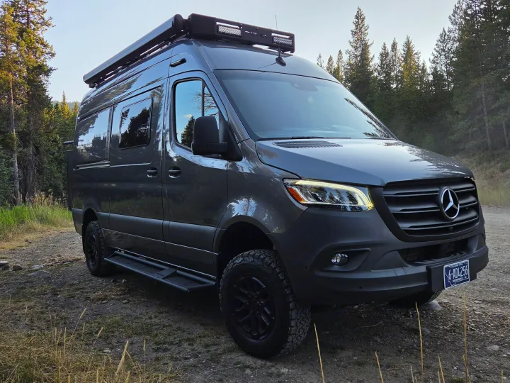 Grey Mercedes-Benz Sprinter adventure van, ready for rv rental. Parked on a dirt path in a scenic Montana forest.. Winnebago Revel 2025