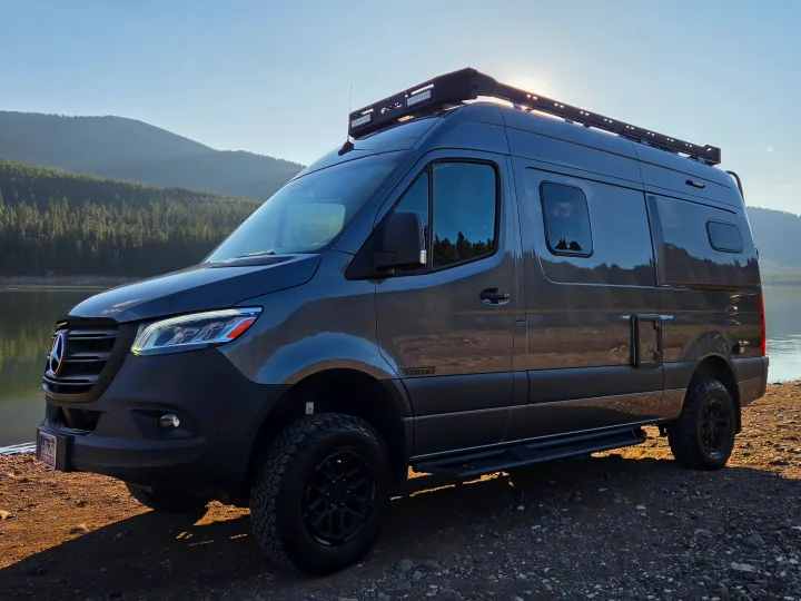 Rugged Winnebago Revel, a Mercedes Sprinter camper van RV rental, ready for adventure by a lake and mountains at sunset.. Winnebago Revel 2025