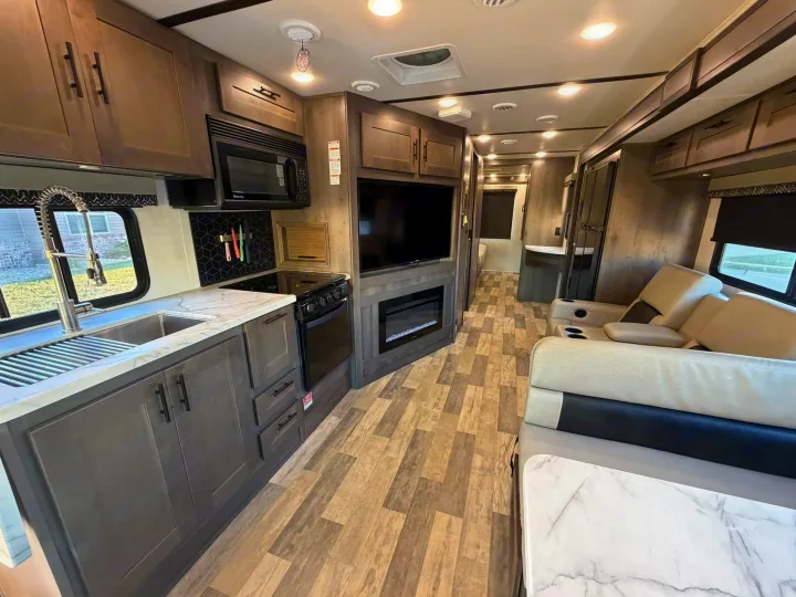 Modern RV rental interior featuring a full kitchen, comfortable living area with TV and fireplace, and wood-look flooring.. FR3 FR3 Motorhome 2022
