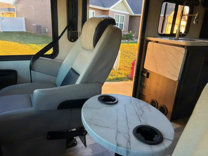 Cozy rv rental interior: a comfy gray passenger seat, marble table with cup holders, and a compact kitchen area.. FR3 FR3 Motorhome 2022