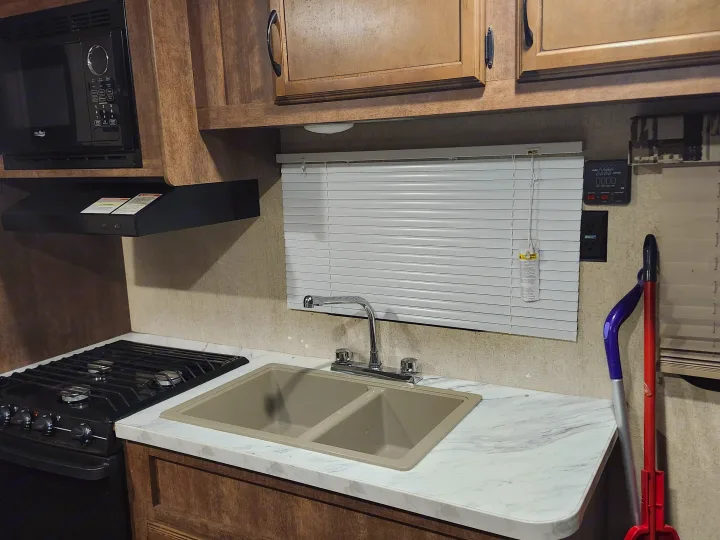RV rental kitchen: microwave, 4-burner stove, double sink, and sleek marble-patterned counter.. Starcraft Autumn Ridge 2018