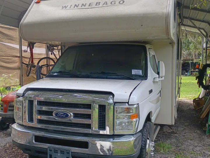A white Ford Winnebago RV motorhome, great for an rv rental, sheltered under a carport with bicycles.. Winnebago Minnie Winnie 2016